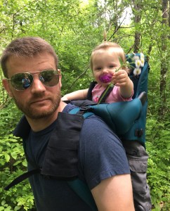 dad hiking with daughter in carrier holding flowers